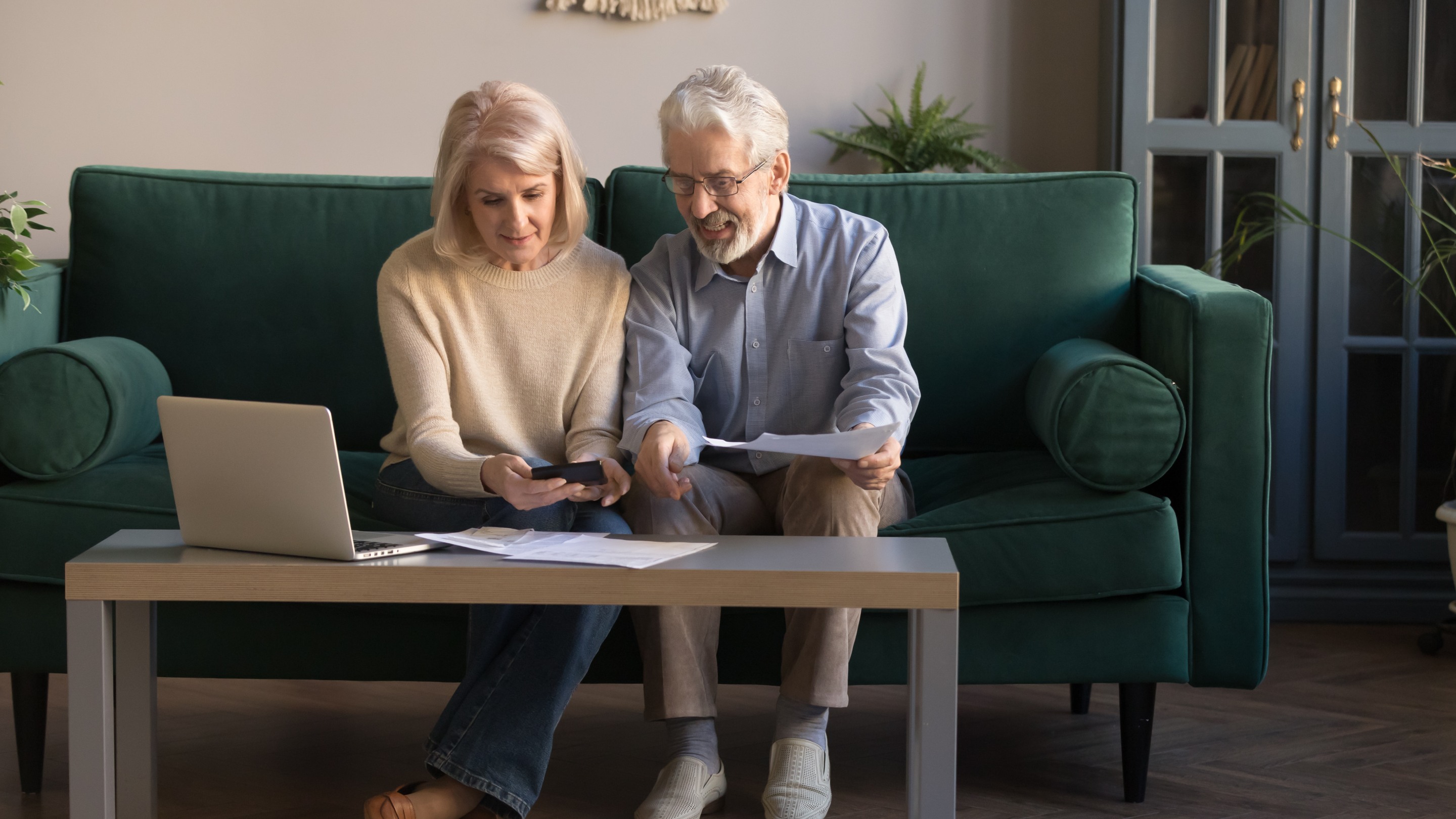 Two people sitting on a sofa at home, reviewing documents together with a laptop on the coffee table.